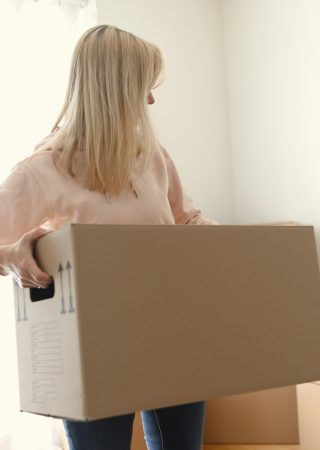 Young woman holding big cupboard box in the room
